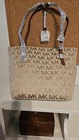 Front view of the beige tote bag with MK logo pattern and wrapped leather straps.