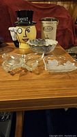 Full view of Mr. Peanut cookie jar, Tim Hortons coffee canister, ruffled edge pottery bowl, glass butterfly dish and floral glass dish arranged on wooden table.