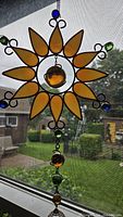 Sun-shaped stained glass suncatcher with amber and blue/green glass beads hung on a window.