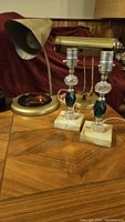 Overview photo of four vintage lamps on wood table: brass desk lamp, ashtray base lamp, two crystal lamps.
