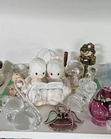 Photo showing a variety of Precious Moments and other assorted glass figurines on a table, featuring a porcelain figurine of two children reading.