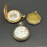 Two pocket watches and one extra watch case on black background. One pocket watch has colorful floral dial and hunter case, the other has Roman numerals and cracked glass. Extra case shows engraved monogram.