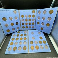 Two blue coin folders showing British halfpennies organized in slots by year and monarch, partially filled and partially empty, coins varying in condition.