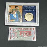 Set includes a commemorative coin with images of Prince Charles and Lady Diana Spencer with accompanying text and a British Armed Forces 5 Pence note in red and green print.