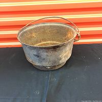 Photo showing the full side view of the cast iron pot with handle, displaying rusty surface and overall condition.
