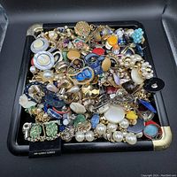 Overview of assorted costume jewelry lot with rings, earrings, brooches, and necklaces in black tray.