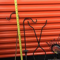 Three tall metal shepherd hooks with candle holders hanging in front of orange storage unit door with measuring tape showing height around 24-30 inches