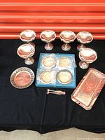 Six silver plated drink cups, four Birks silver plated coasters in packaging, small round pierced edge tray, elongated rectangular tray, and sugar tongs