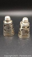 Pair of sterling silver salt and pepper shakers with pierced cutout designs and smooth tops with holes.