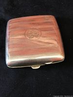 Front view of vintage silverplate cigarette case showing horizontal striped pattern and monogram engraving.