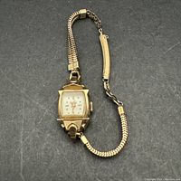Photo of the front of the vintage ladies Benrus wristwatch showing square gold-tone case, off-white dial, and expandable bracelet