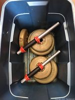 Weight plates and two bars inside a gray container, showing 5lb and 10lb plates with red collars on bars