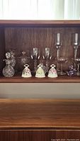 View of entire collection including glass decanter, jar with lid, vases, stemmed glasses, and three ceramic floral bells