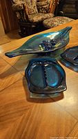 Elongated blue glass leaf bowl and two rectangular divided dishes on wood table with floral carpet visible