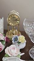 Close-up of vintage-style gold clock and several china flower arrangements on display next to the crystal basket.