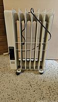 Front view of beige Delonghi radiator heater with six fins and power cord wrapped around one fin.