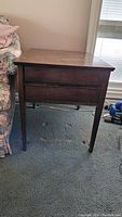 Front view of a dark brown wooden end table with two closed drawers showing intact structure but surface wear marks