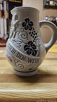 Close-up of traditional German ceramic beer stein featuring grapevine and German text decorations
