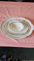 Photo of all 5 pieces stacked showing large oval platter and 4 nested serving bowls on pink textile surface.
