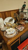 Photo showing a variety of decorative items including horse-themed plates, horse figurine, vases, and coaster sets arranged on wood furniture.