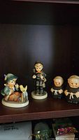 Group photo showing three vintage Hummel porcelain items on shelf: figurine and two salt and pepper shakers.