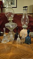 Full view of two glass hurricane lamps and six assorted glass bells on wooden surface.