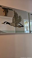 Close-up view of the central section of the mirrored glass art piece showing the crafted colored glass mallard duck with wings spread in flight.