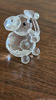 Clear faceted Swarovski crystal baby elephant figurine angled showing trunk, black eyes, ears, spherical feet on wood surface