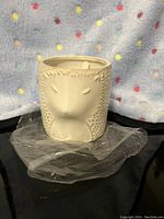 White ceramic animal-shaped candle holder with animal features and textured fur detail, placed on plastic.