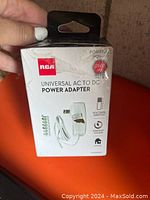 Photo showing RCA Universal AC to DC Power Adapter box with product features including voltage switch, energy saver, portable power, and multiple interchangeable tips.