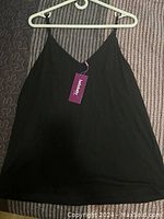 Front view of the black loose fit tank top hanging on a hanger, showing the full front area and general fit.
