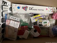 Overview of the DIY diamond painting kit box with assorted colorful craft items including stickers, ribbons and tools beneath it.