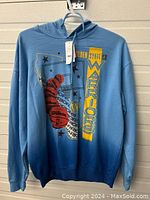 Full front view of light blue Golden State Warriors hoodie with graphics and tags visible.