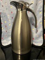 Front view of the stainless steel hot beverage holder showing shape, finish, handle, and lid position.