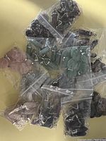 Overview of multiple small sealed bags containing stone pendants in assorted colors including purple, green, and pink.