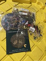 Four outdoor decor items in original packaging: a round metal plate with a dragon or phoenix design, a colorful hanging decoration with flower shapes and beads, a metal branch with leaves, and an artistic stainless steel wind spinner in box with tree of life design.