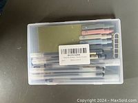 Top view of a transparent plastic box with multiple pens and pen refills in various colors along with a small ruler and clip inside.