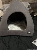 Gray fabric pet bed tent with triangular entrance and white interior cushion.