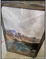 Framed mountain landscape poster wrapped in clear plastic showing the frame and poster inside.