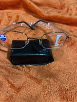 Folding reading glasses placed on top of black protective case against orange fabric background.