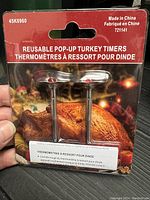 Photo of packaged reusable pop-up turkey timers with two timers visible and packaging showing product details and cooked turkey image