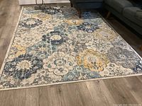 Photo showing the full view of the area rug on a wooden floor next to a gray sectional couch.