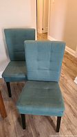 Two teal upholstered dining chairs front view showing grid-stitched upholstery and slightly worn seats.