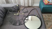 Metal wall clock and round mirror on sofa.