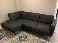 Dark gray fabric sectional sofa with wooden legs captured from front angle showing both couch and chaise lounge section clearly.