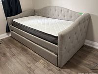 Side angle view of the assembled upholstered day bed with tufted backrest and pullout bed underneath with two mattresses, showing overall condition and fabric color.