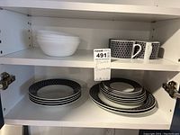 Dishes and mugs inside white cupboard with plates, bowls, and mugs marked with maxsold tag 491