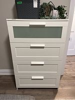 Front view of white melamine dresser showing four drawers, top drawer has a frosted glass panel insert, wide rectangular handles and smooth finish.