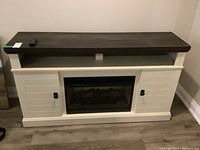 Full frontal view of console showing dark brown top shelf, off-white body, side cabinets, and remote on left edge.