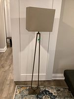 Full view of metal floor lamp with beige rectangular shade against white wall.